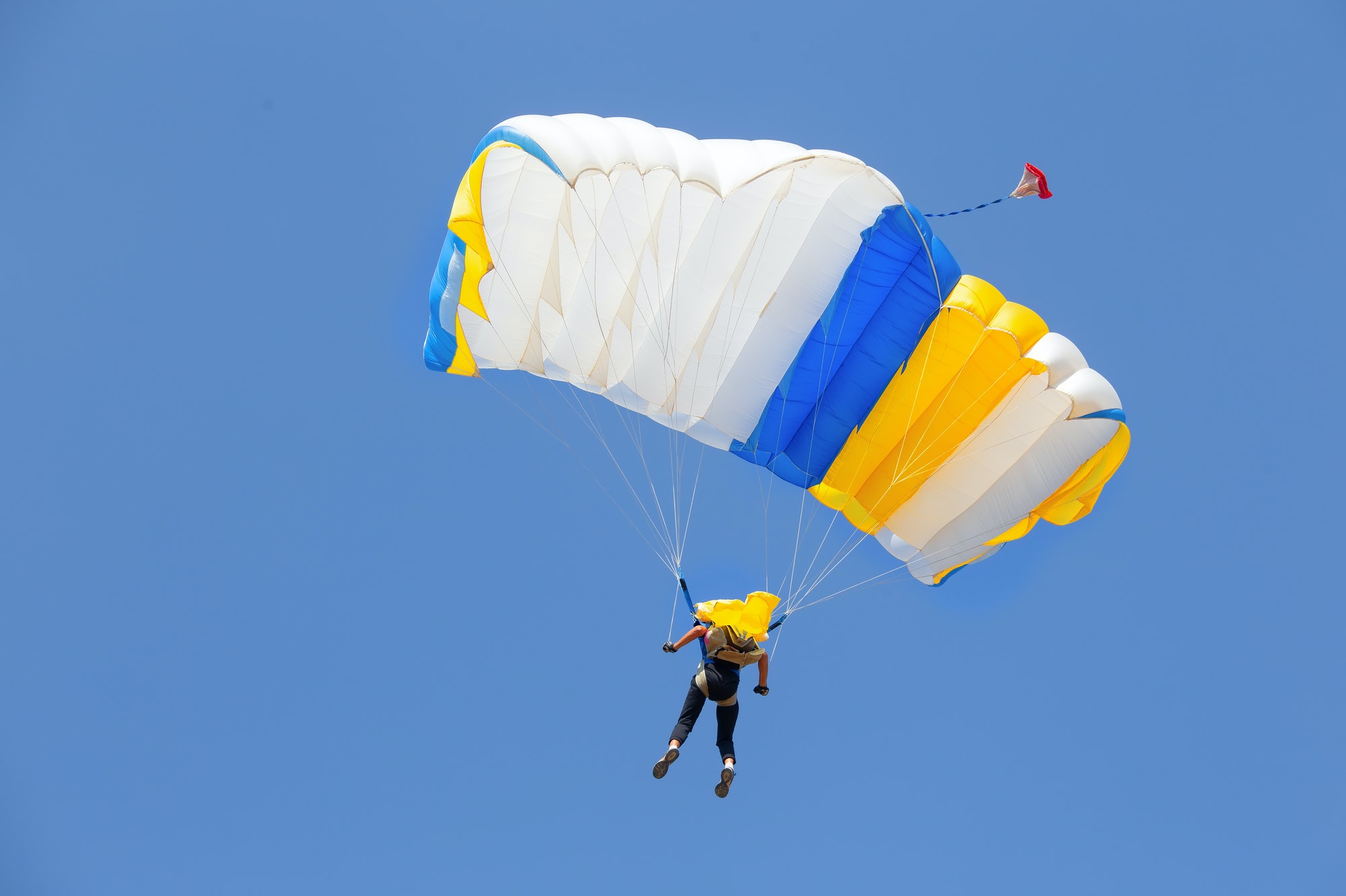 skydiver-under-canopy-of-yellow-with-blue-parachute-in-cloudless-sky